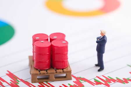 Miniature people : Business standing in front of drum and see the trend of oil The background is US dollar. Price oil down. Barrel arrow down. Business and finance concept.の写真素材
