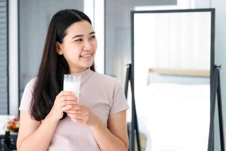 Young Asia woman drinking milk in the bedroom. Feeling happy smile and refreshment on the first meal in the morning. Healthy and refreshment concept.の写真素材