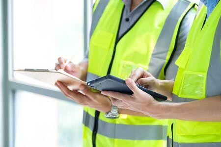 Two engineers man standing in front of windows and used tablet to find construction model. Working...