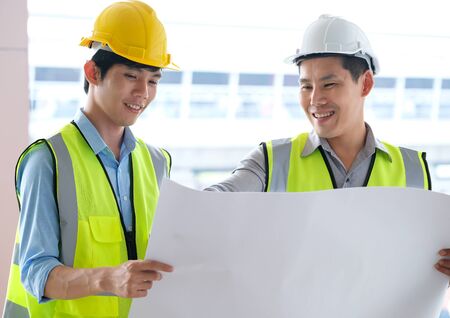 Two engineers man standing in front of the site. Left engineer holding blueprint diagram and right engineer point his hand to  drawing diagram in blueprint. Engineering and construction concept.の写真素材