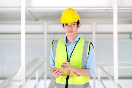Junior engineer standing in the plant holding the clipboard and pencil with copy space. Wearing...
