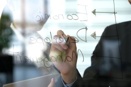 Asia young businessman write some word on the transparent glass board in the modern office and explain to business women. Focused on black pen. Business and marketing concept.の写真素材