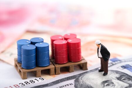 Miniature people : Senior engineer standing on the banknote (US dollars and Singapore dollars) with banknote and oil drums background and think how to manage oil stock. Money, business and finance conceptの写真素材