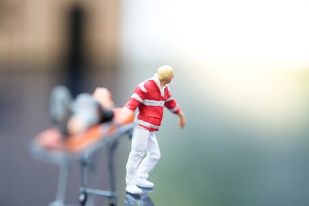 Miniature people : Injured man lying on the first aid bed and there is emergency medical staff dragging a first aid bed. Focused on emergency man. Emergency, life insurance, accident concept.の写真素材