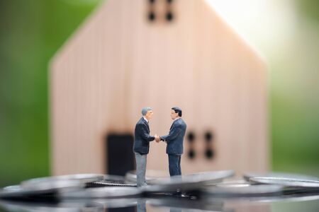 Miniature people : Two businessmen standing in the coin and shake hand and deal business on selling house with blurred background. Property Business, financial and Strategy Planning concept.の写真素材