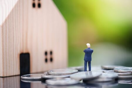Miniature people : Businessman standing on the coin and planning to buy house under sunlight with blurred background. Property Business, saving, financial and Strategy Planning concept.の写真素材