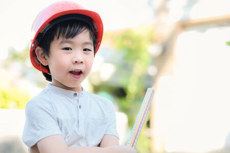 Young Asia boy in gray T shirt wearing a orange safety helmet and holding triangular reduction scales in the garden at home. Feeling happy, fun and smile. Engineering and learning education concept.の写真素材