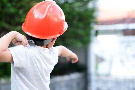 Young Asia boy in gray T shirt wearing a orange safety helmet stand in the garden at home under sunlight. Feeling angry and unhappy. Point his hand out. Engineering and learning education concept.の写真素材