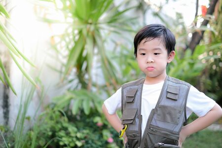Curious little young Asian boy standing in the garden. Exploring the world, outdoors activity. Feeling fun and happy. Boy wear green outdoors vest. Holiday, education conceptの写真素材