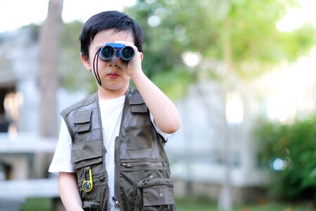 Curious little young Asian boy looking through a binoculars in the garden. Outdoors activity....