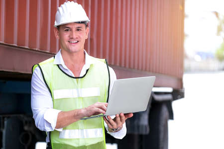 Engineer worker or technical standing in the container yard shipping area and used a laptop or computer to control loading containers into the truck. Industrial and import-export conceptの写真素材