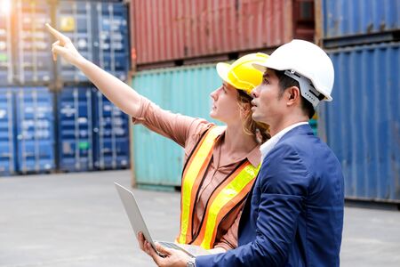 Engineer worker and businessman standing in the container cargo shipping area. Women point to...