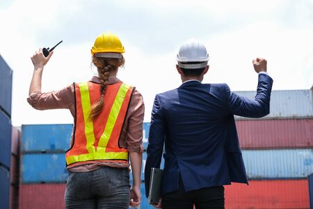 Back view of engineer worker holding the walkie talkie and boss holding laptop raise hand up in the container cargo shipping area. Successful of work. Import and export logistic transportation conceptの写真素材
