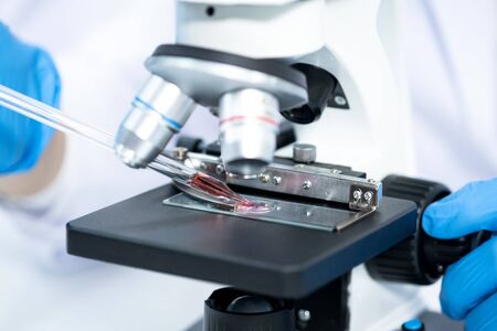 Asia young scientist using a microscope to see coronavirus (Covid-19) in a laboratory. He drops the dilution of blood samples in the glass. Researchers find a vaccine to prevent the virus.の写真素材