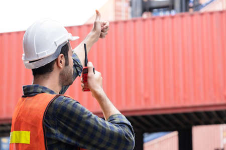 Engineer worker or technical standing and thumb up in the container yard shipping area and used radio communication to control loading containers into the stack. Industrial and import-export conceptの写真素材