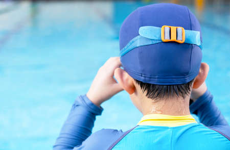 Boy wearing goggles and sit at the edge of the pool swimming. Prepare the body before jump into the pool. Summer children's sports activity with a parent. Learning and relaxation concept.の写真素材