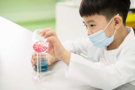 Elementary school student doing a science experiment. A boy pouring pink solution from breaker into the cylinder and feeling happy and fun on the mixing of the solution. Experiment concept.のeditorial素材