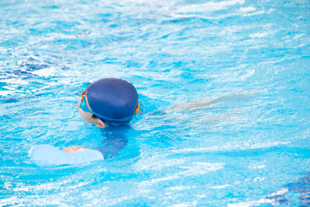 Asia cute boy wearing swimming suit and goggles used foam to practice swimming in swimming pool. Healthy kid enjoying active lifestyle. Refreshing and relax to exercise on summer holidayの写真素材