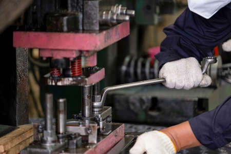 Engineer or worker wearing a helmet, mask and safety glasses using wrench to screw nut at the CNC machine. Working in manufacturing, factory. Concentrate on work. Maintenance, repair conceptの写真素材