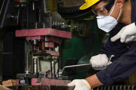 Engineer or worker wearing a helmet, mask and safety glasses using wrench to screw nut at the CNC machine. Working in manufacturing, factory. Concentrate on work. Maintenance, repair conceptの写真素材