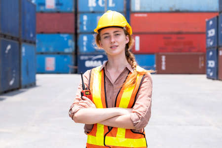 Confident of a businesswoman wearing a safety helmet holding walkie talkie in the container yard...
