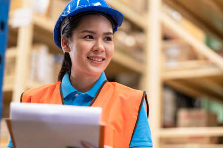 Woman worker holds clip charts and takes notes in the large warehouse distribution store. Female...