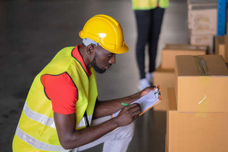 A Man worker writing address from the parcel on paper on the clipboard in the large warehouse...