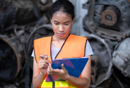 Africa American engineer woman worker holding tablets and take note. Standing in the automotive spare parts warehouse. Maintainance and service concept. Many old engines. Concentrate on the job.の写真素材