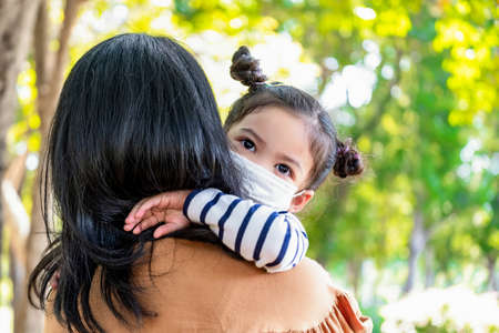 Asia cute girl (daughter) hugging mom in the garden on blurred background. Kid wearing hygiene...