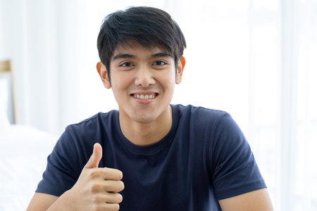 Attractive Asia man thumb up sitting on the living room and conference meeting via laptop.  Technology, meeting or teaching concept. Work from homeの写真素材