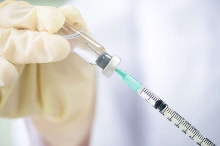 Scientist or doctor hand wear medical glove and filling solution of vaccine liquid into syringe....
