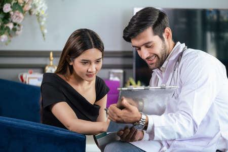 Woman discuss with confident doctor who wear lab coat and sitting on sofa at the modern beauty clinic. Beautiful female sign contract before do plastic surgery. Beauty and service conceptの写真素材