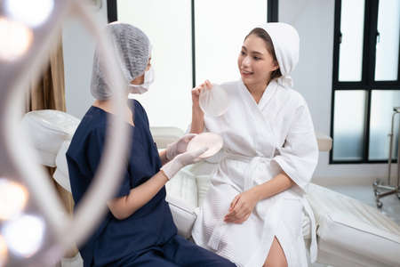 Beautiful woman sitting on the bed in the surgery room with professional at the modern clinic....
