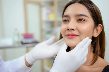 Beautician doctor wear glove touch female face and check skin condition before plastic surgery in the beauty clinic. Woman going under cosmetic treatment on her facial skin. Service and enhancementの写真素材