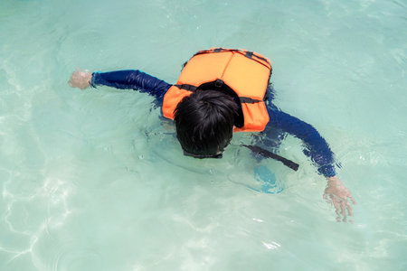 Asia child boy wearing goggles, swimming suit and life jacket snorkelling in the sea at beach in Thailand with copy space. Summer vacation and holiday travel. Relaxation and happy in the waterの写真素材