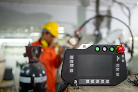 Close up of remote control for robotic arm machine to work in the factory. Blur background of worker setup program on the remote to do welding metal. Technology and industrial 4.0 concept.の写真素材