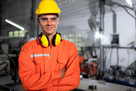 Portrait of young engineer standing and work in the robot factory. Wearing orange uniform, safety...