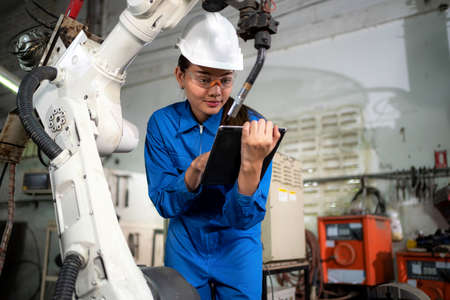 Engineer woman looking at tablet and see how to operate robotic arm machine in the factory. Worker...