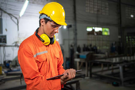 Engineer man in uniform holding tablet and check robotic arm machine standing in the factory. Worker...