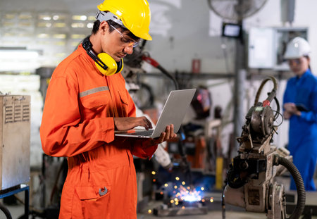 Engineer man use laptop to control welding robotic automatic arm machine in the smart factory....