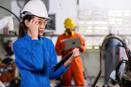 Engineer woman use tablet to control welding robotic automatic arm machine in the smart factory....