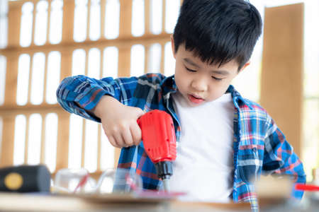 Young Asia boy wearing T shirt and concentrate to use screwdriver toy in the classroom or workplace. Many equipment on the table. Repairing, builder, handcrafting concept. Education and learningの写真素材