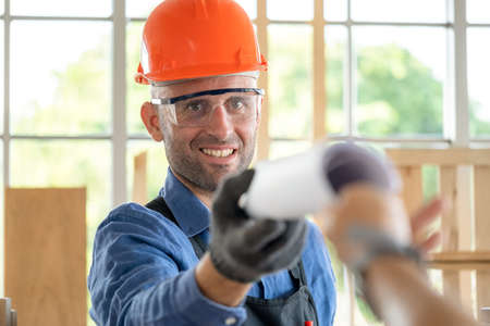 Professional carpenter wearing goggle and safety helmet receive blueprint or furniture diagram from...