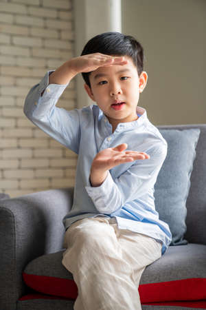 Asia boy wearing blue shirt, cross legged and sitting on the sofa in the living room with copy space...