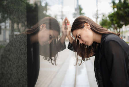 Side view of depressed bored businesswoman standing in front of office building and put her hand on...