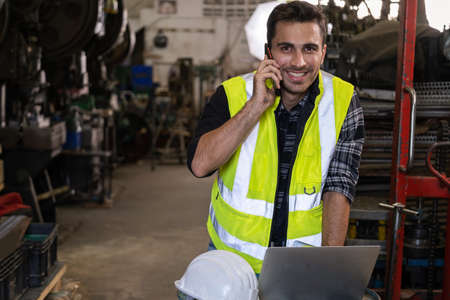 Technical engineer wearing safety vest standing in the factory workplace. Worker using smartphone...