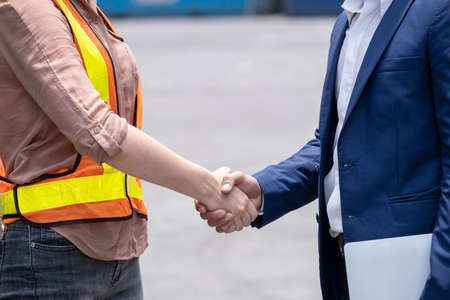 Engineer worker wearing safety vest standing at shipping container terminal and shake hand with manager. Working in transportation goods in the shipping yard. Industrial and logistic conceptの写真素材