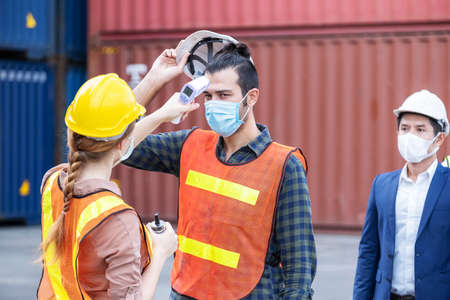 Female engineer worker scanning to check temperature of staff before entering to the container construction site by using digital thermometer. Wearing hygiene face mask. New normal conceptの写真素材