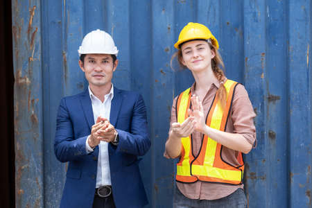 Engineer worker wearing safety vest standing at shipping container terminal and clapping hand with manager. Working in transportation shipping yard. Successful work. Industrial and logistic conceptの写真素材
