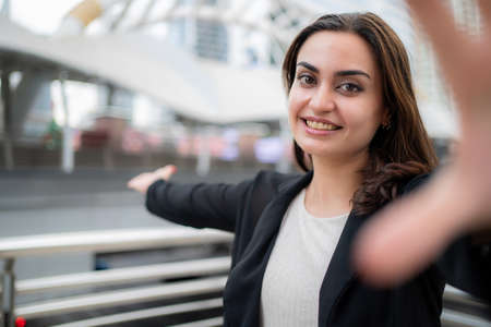 Pretty businesswoman wearing suit touch a camera and introduce the business area with copy space. Worker feeling happy and smile in the job. Business outdoor and lifestyle concept.の写真素材